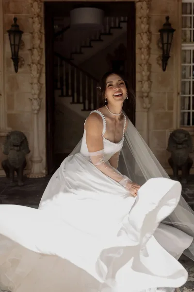 Bridal portrait of a bride laughing in a flowing gown with a long tulle veil on a stone staircase between lantern sconces and statues.
