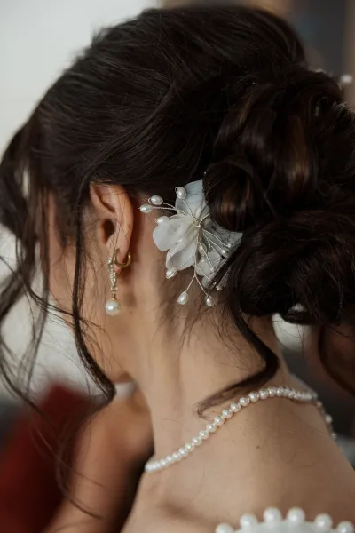 Bridal updo in a polished low bun wedding hair, accented by a pearl hairpin and soft face-framing tendrils.