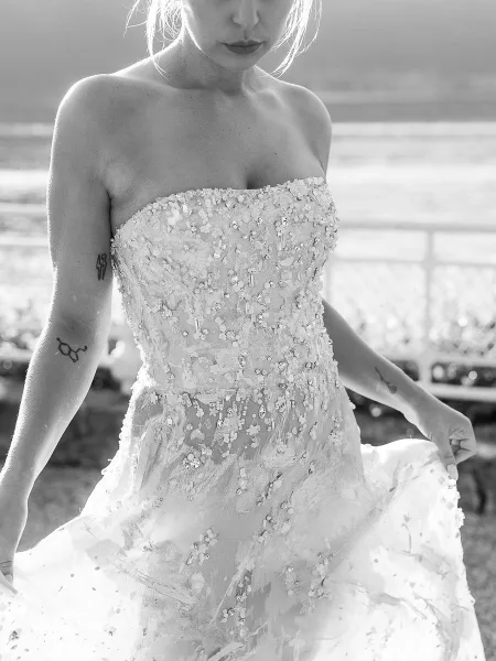 Wedding dress close-up of a strapless wedding dress with beaded appliqué bodice and tulle skirt, set against water and distant hills