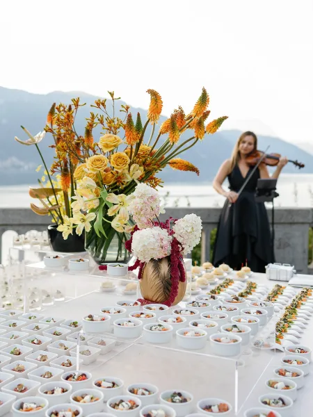 Wedding cocktail hour appetizer display with passed bites, mini bowls and florals on a stone terrace overlooking a lake and mountain view