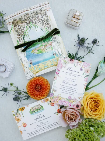 Invitation suite with watercolor wedding invitation cards, velvet ribbon, rings and floral accents arranged on a linen fabric backdrop