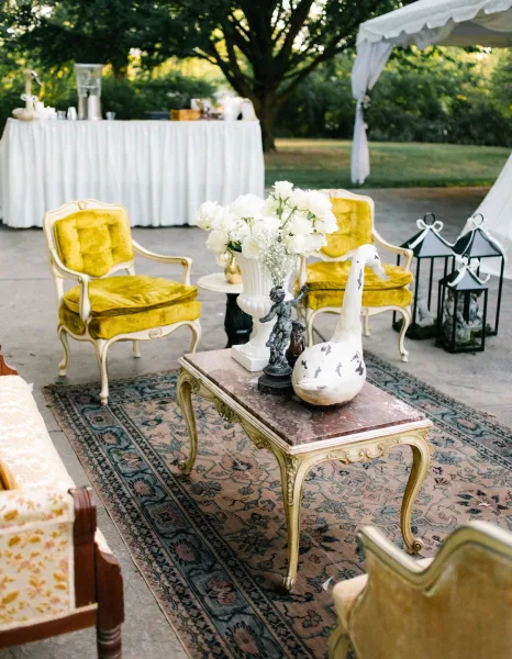 Wedding lounge decor creates inviting outdoor lounge seating with velvet armchairs under a garden tent amid trees on the grass lawn.