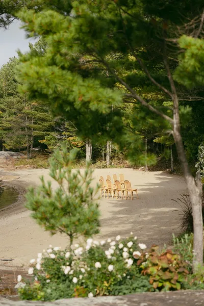 Ceremony seating with beach ceremony chairs in neat rows, accented with simple florals, set on a sandy lakeshore framed by pine trees.