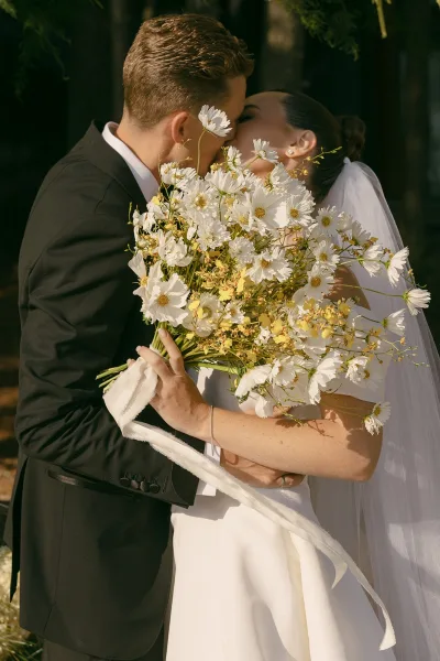 Wedding kiss portrait of a bride and groom kiss in a soft newlywed embrace, her veil catching the light as they share a tender moment.