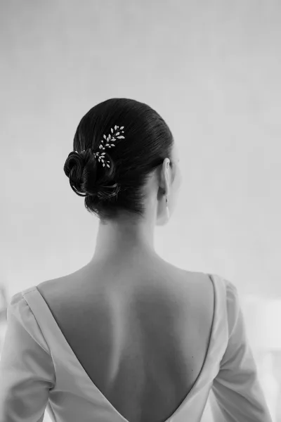 Bridal updo styled as a sleek low bun, accented with a delicate hair pin for a refined, minimalist look.