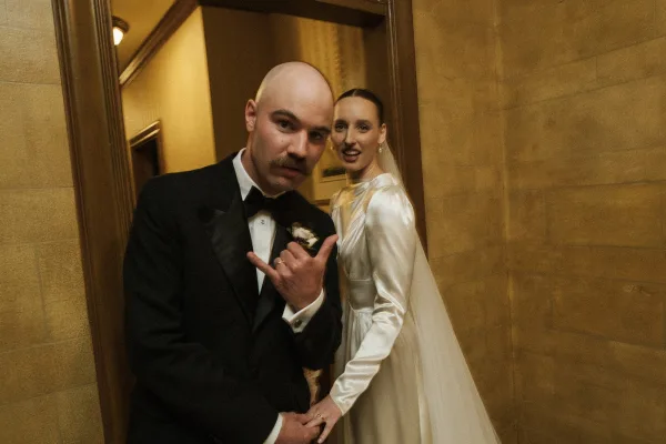 Couple portrait in a candid wedding photo, bride and groom holding hands in a wood-trimmed doorway, her veil catching light.