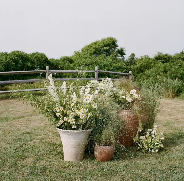 Wedding floral arrangements with wildflower ceremony flowers in a ceramic planter, white blooms and greenery on a lawn by a wooden fence
