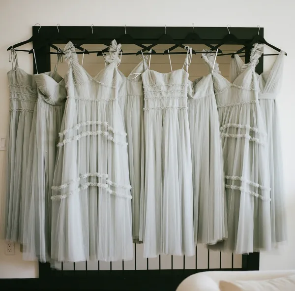 Bridesmaid dresses in mismatched bridesmaid dresses palette hanging on a rack, with tulle and spaghetti straps in a bright bedroom setting