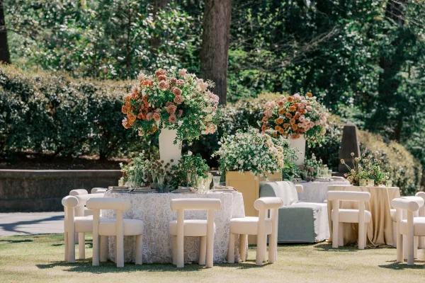 Reception tablescape for outdoor reception decor, featuring lush floral centerpieces beside garden hedges and a stone wall.