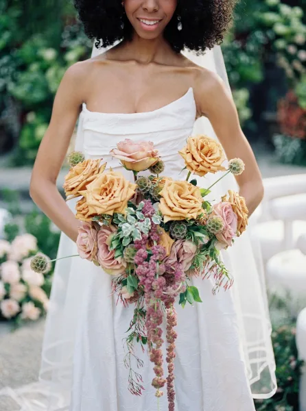 Bridal bouquet in a cascading bouquet style with trailing amaranthus, framed by lush garden greenery and a stone path.