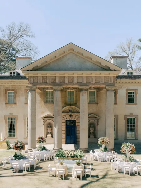 Outdoor reception decor featuring pastel floral centerpieces for a courtyard wedding reception beside a mansion facade with stone columns.